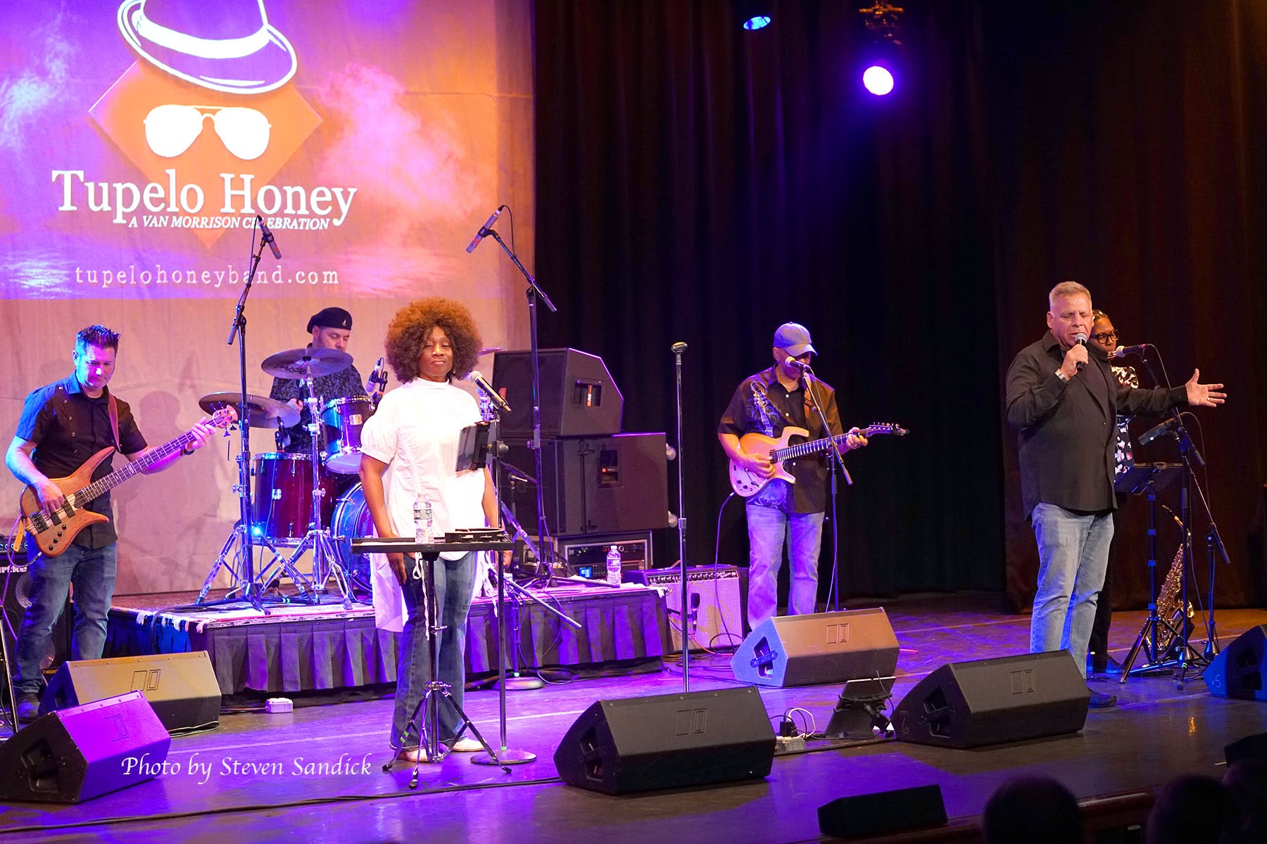 Full band performing with Tupelo Honey stage banner